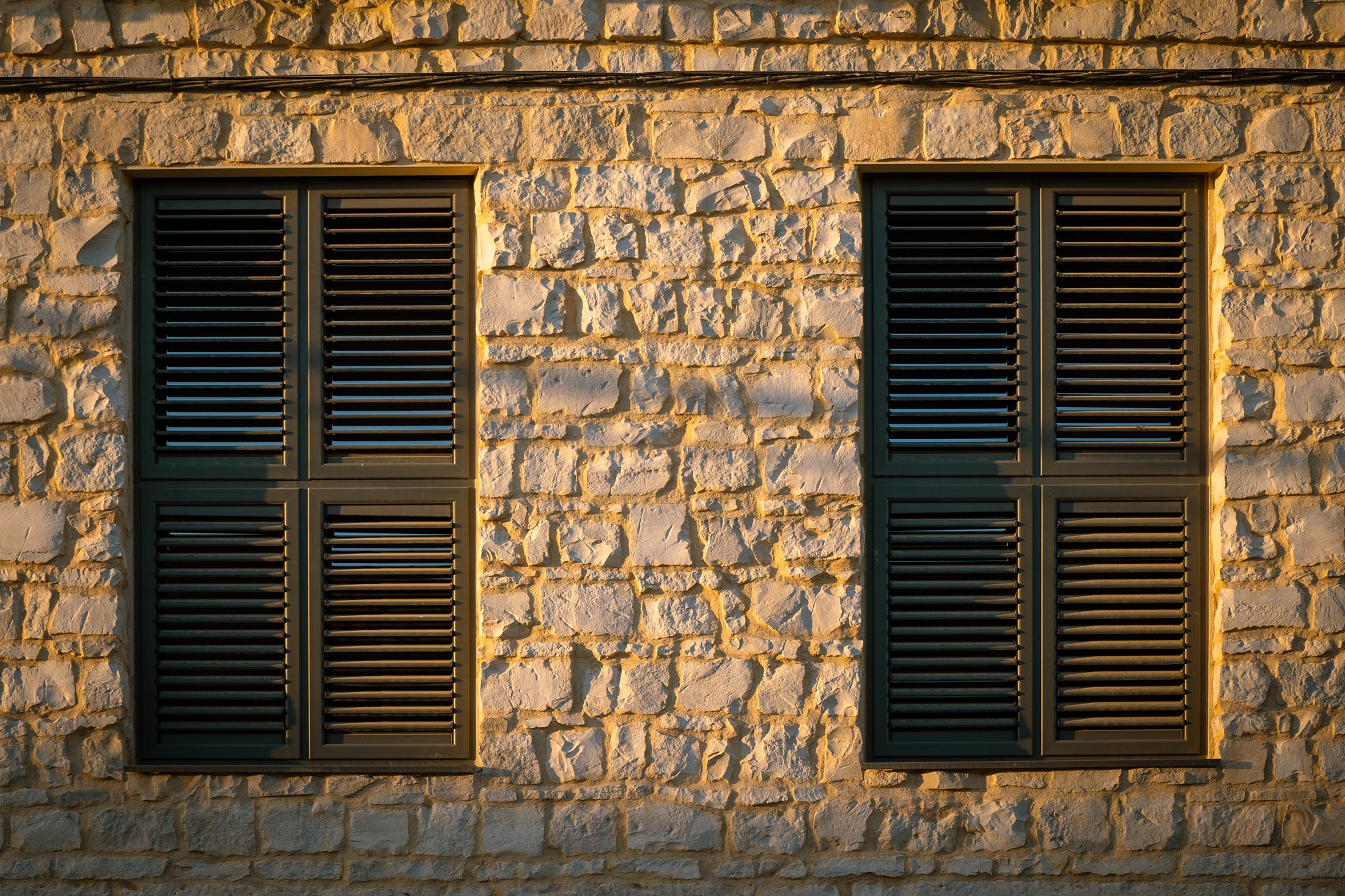 Primer plano de dos ventanas con contraventanas de librillo oscuras integradas en el muro de piedra